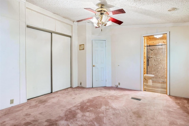 unfurnished bedroom featuring ceiling fan, light carpet, a textured ceiling, and ensuite bath