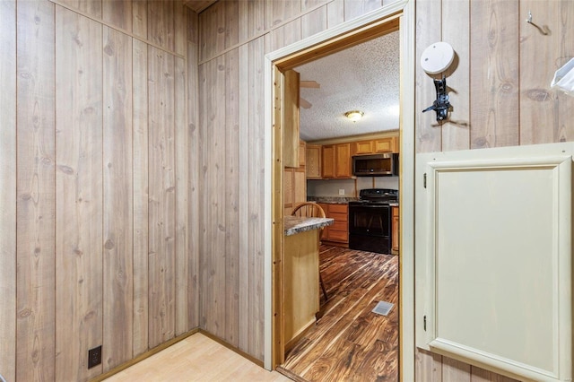 corridor featuring wooden walls, a textured ceiling, and light hardwood / wood-style floors