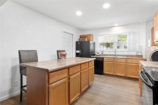 kitchen with sink, a kitchen island, black appliances, and light hardwood / wood-style flooring