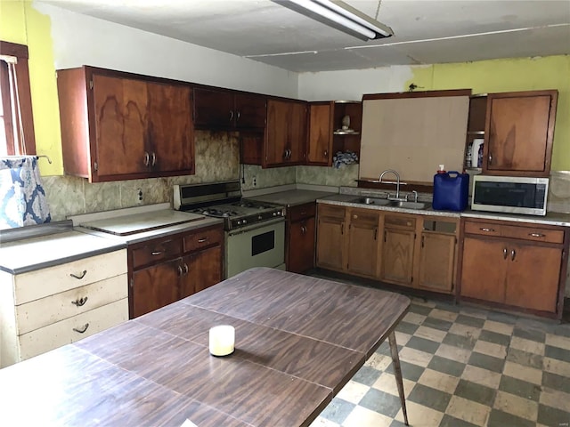 kitchen with a sink, light countertops, tile patterned floors, stainless steel microwave, and white gas range