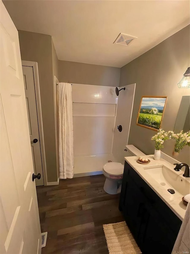 bathroom with hardwood / wood-style floors, walk in shower, vanity, and toilet