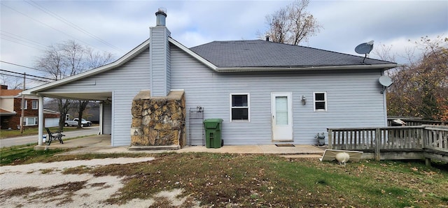 rear view of property with a deck, roof with shingles, a chimney, and a carport