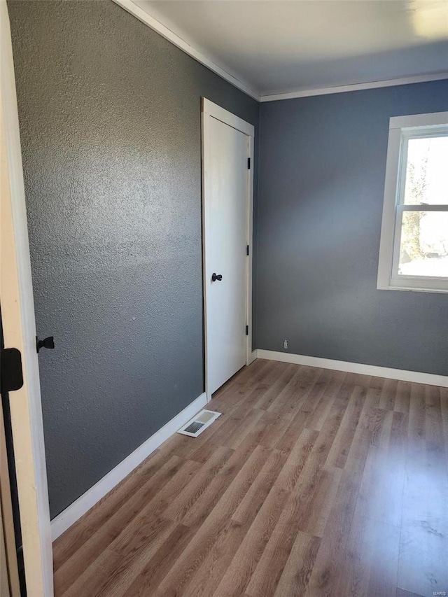 empty room featuring baseboards, visible vents, a textured wall, ornamental molding, and wood finished floors