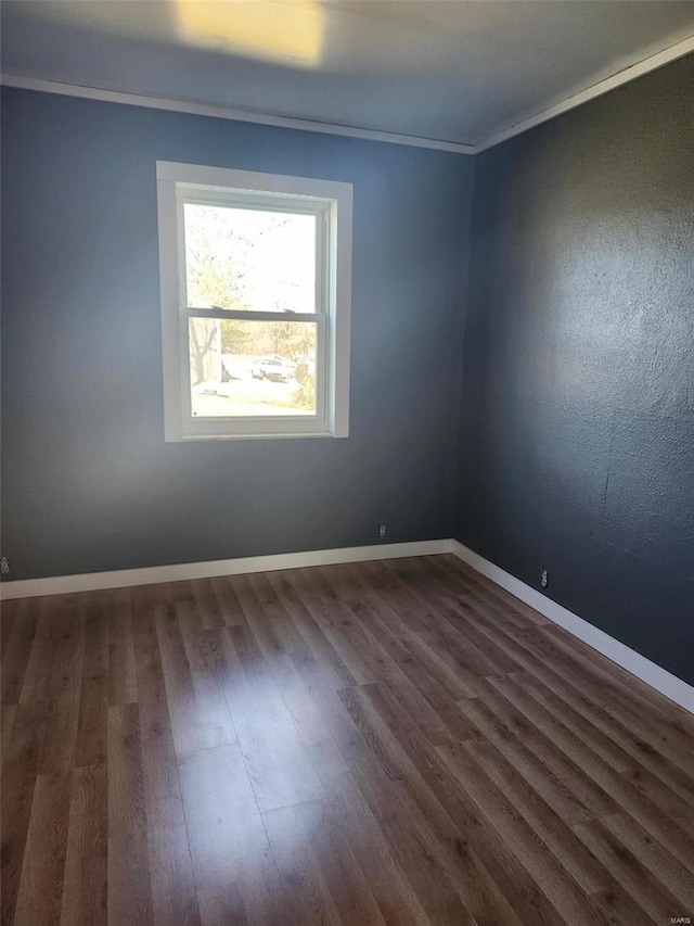 empty room with dark wood-style floors, crown molding, and baseboards