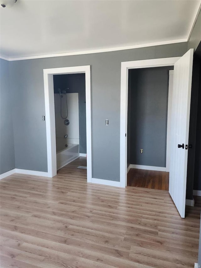 spare room with baseboards, crown molding, and light wood finished floors