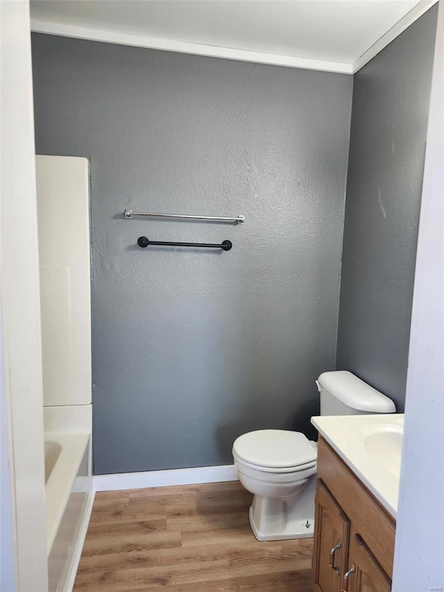 full bath with a textured wall, toilet, vanity, wood finished floors, and baseboards