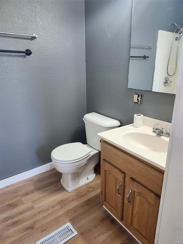 bathroom featuring visible vents, toilet, vanity, wood finished floors, and baseboards