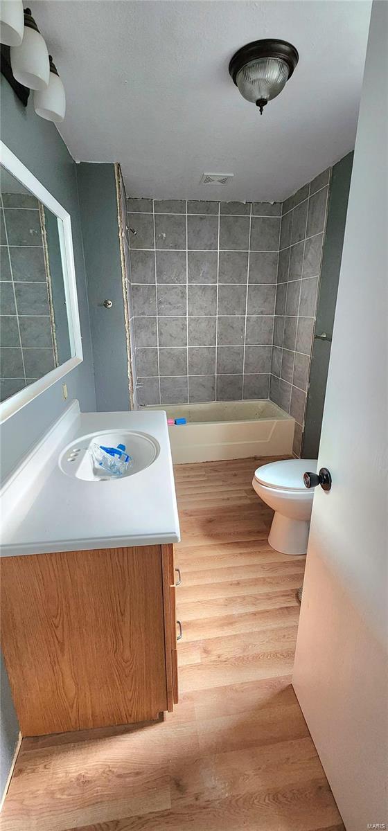 full bath featuring toilet, visible vents, wood finished floors, and vanity