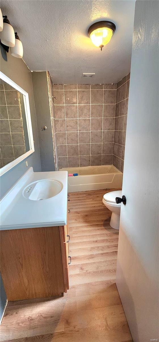 full bath featuring visible vents, toilet, vanity, a textured ceiling, and wood finished floors