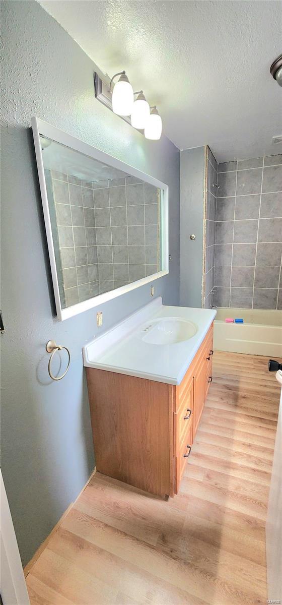 bathroom with a textured ceiling, bathing tub / shower combination, wood finished floors, and vanity