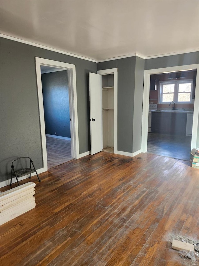 unfurnished bedroom featuring a sink, wood-type flooring, baseboards, and crown molding