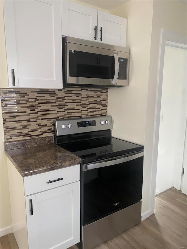 kitchen with backsplash, stainless steel appliances, white cabinetry, and light hardwood / wood-style floors