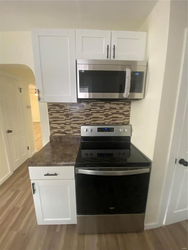 kitchen with white cabinets, appliances with stainless steel finishes, light wood-type flooring, and tasteful backsplash