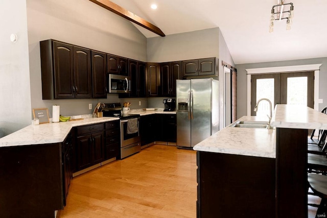 kitchen featuring vaulted ceiling with beams, sink, light wood-type flooring, appliances with stainless steel finishes, and dark brown cabinetry