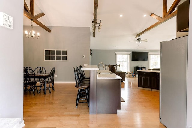 kitchen featuring sink, light wood-type flooring, a breakfast bar area, stainless steel fridge, and pendant lighting