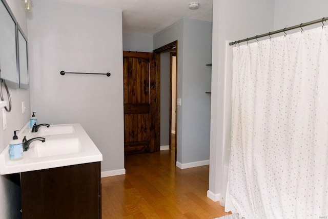 full bath with curtained shower, a sink, wood finished floors, baseboards, and double vanity