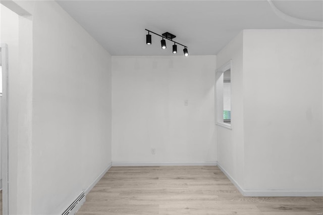 empty room with light hardwood / wood-style flooring, a baseboard heating unit, and rail lighting