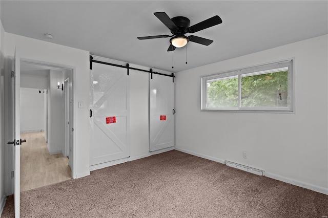 unfurnished bedroom with ceiling fan, a barn door, baseboard heating, and light colored carpet