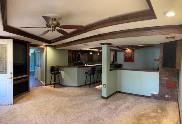 kitchen featuring light carpet, ceiling fan, a breakfast bar area, a tray ceiling, and crown molding