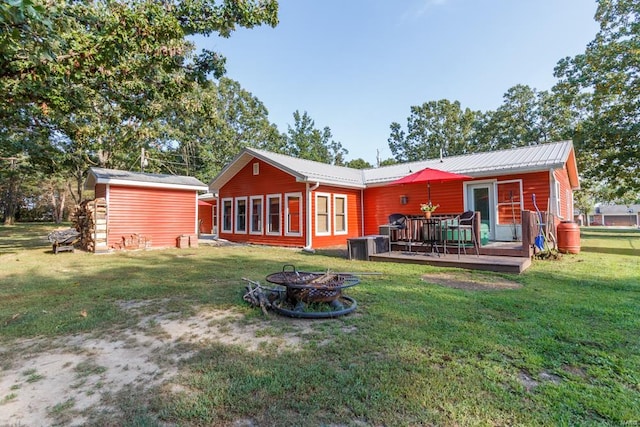 rear view of property featuring a fire pit, a deck, a lawn, and a storage unit