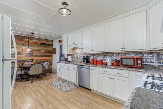 kitchen featuring white cabinets, light wood-type flooring, stainless steel appliances, and wood walls