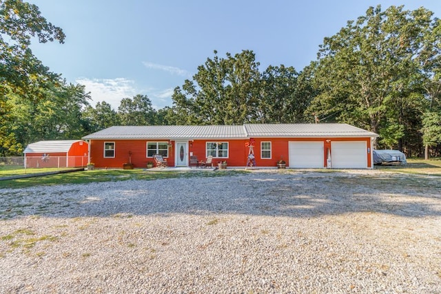 ranch-style house with an attached garage, metal roof, gravel driveway, and fence