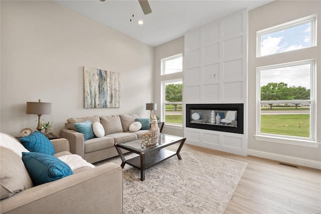 living room with ceiling fan, light wood-type flooring, a wealth of natural light, and a fireplace