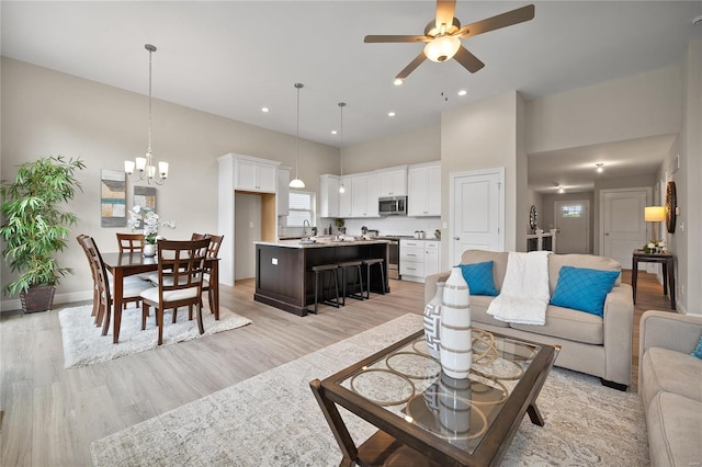 living room with sink, a towering ceiling, light hardwood / wood-style flooring, and ceiling fan with notable chandelier