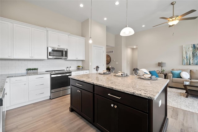 kitchen with light hardwood / wood-style flooring, ceiling fan, appliances with stainless steel finishes, a center island, and backsplash