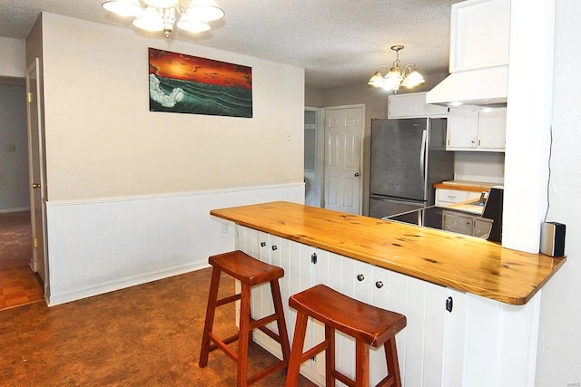 kitchen with white cabinets, dark tile patterned flooring, an inviting chandelier, decorative light fixtures, and stainless steel refrigerator