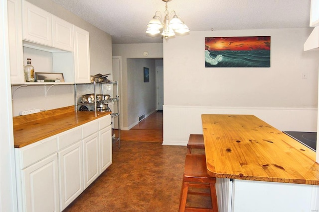 kitchen featuring pendant lighting, wood counters, a notable chandelier, black electric stovetop, and white cabinetry