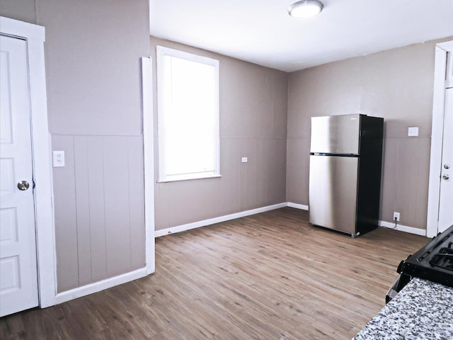 kitchen featuring electric range oven, stainless steel fridge, wood-type flooring, and light stone countertops