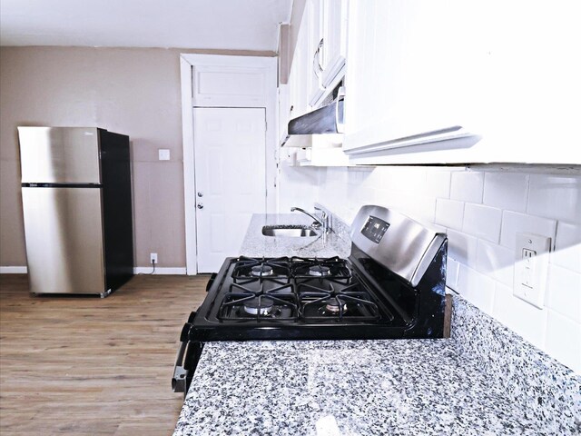 kitchen with gas range, light hardwood / wood-style floors, white cabinetry, stainless steel refrigerator, and sink