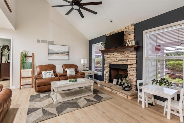 living room featuring a fireplace, light wood finished floors, visible vents, a ceiling fan, and high vaulted ceiling