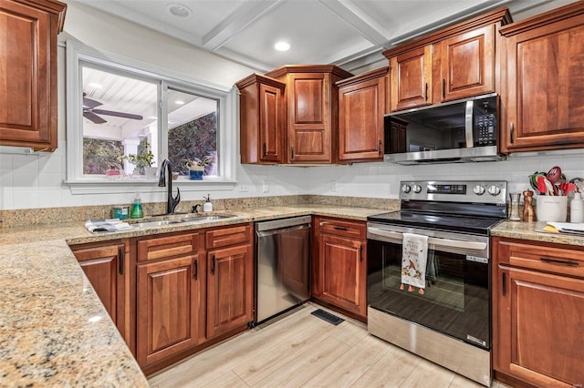 kitchen with ceiling fan, light stone counters, stainless steel appliances, a sink, and decorative backsplash