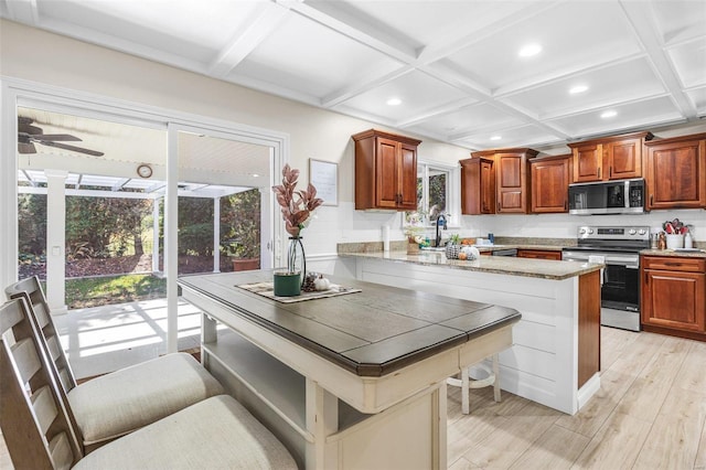 kitchen with appliances with stainless steel finishes, coffered ceiling, plenty of natural light, and a breakfast bar area