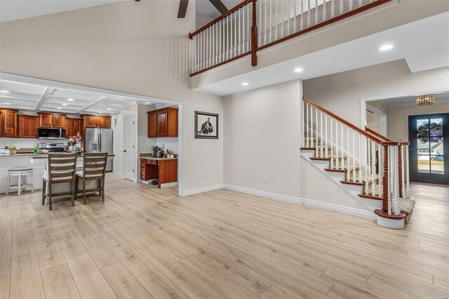 living room with baseboards, a ceiling fan, light wood-style flooring, stairway, and a high ceiling