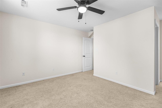 spare room with a ceiling fan, light colored carpet, and baseboards