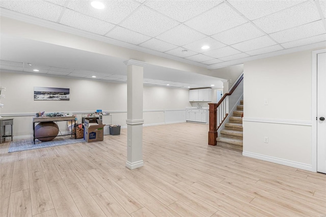 finished basement with light wood-style floors, stairs, baseboards, and a drop ceiling