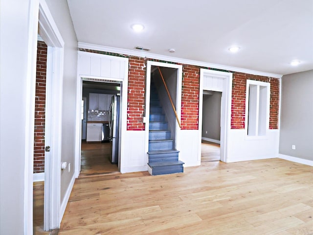 interior space featuring light hardwood / wood-style floors, brick wall, and ornamental molding