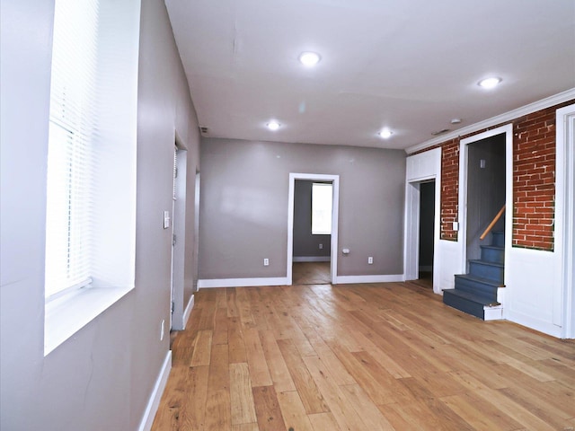 spare room with light wood-type flooring, ornamental molding, and brick wall