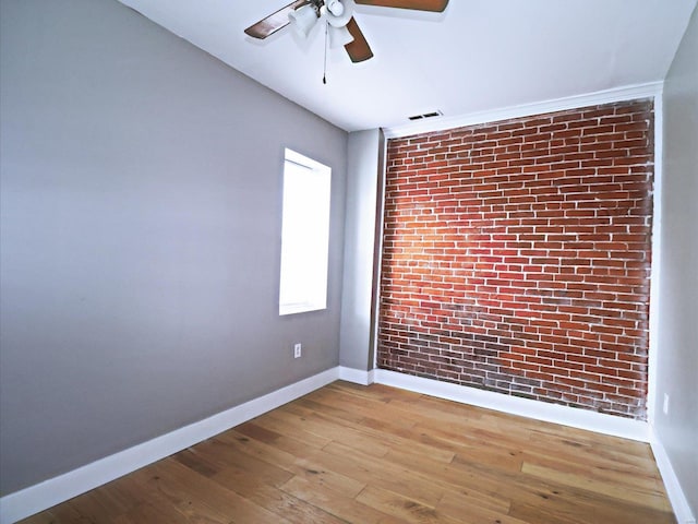 spare room featuring ceiling fan, light hardwood / wood-style flooring, and brick wall