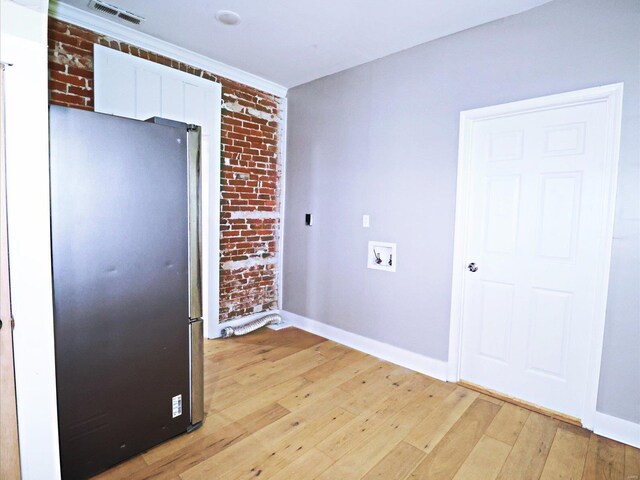 kitchen with light wood-type flooring, brick wall, refrigerator, and white cabinetry