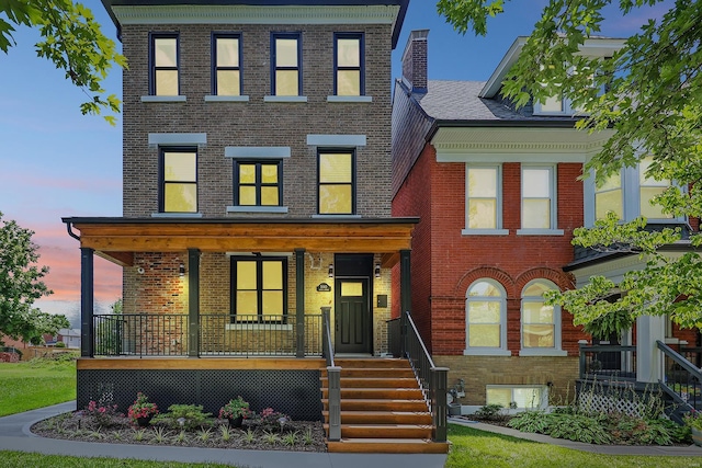 view of front of home with covered porch, a chimney, and brick siding