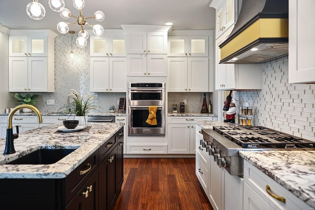 kitchen with wall chimney range hood, pendant lighting, backsplash, stainless steel appliances, and sink