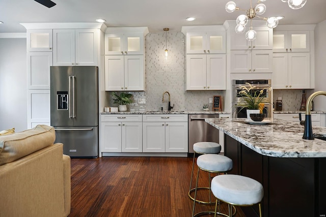 kitchen with appliances with stainless steel finishes, backsplash, white cabinets, dark hardwood / wood-style floors, and decorative light fixtures