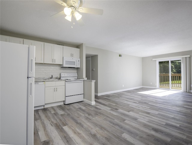 kitchen featuring white appliances, a sink, white cabinets, open floor plan, and tasteful backsplash