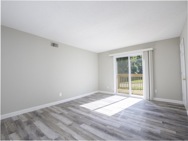 empty room featuring visible vents, baseboards, a textured ceiling, and wood finished floors