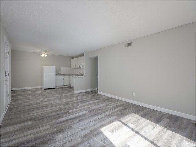 unfurnished living room with ceiling fan, visible vents, baseboards, and light wood-style flooring