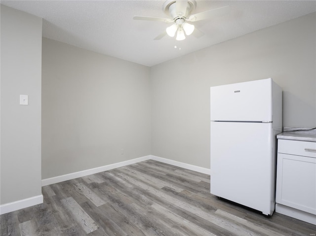 interior space with white cabinetry, wood finished floors, baseboards, and freestanding refrigerator